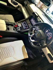 Interior of a luxury car featuring a sleek black and white two-tone design. The dashboard includes a touchscreen display, digital speedometer, and various controls. The steering wheel has a logo, and the seats are upholstered with a geometric pattern.