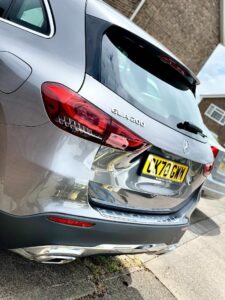 A silver Mercedes-Benz GLA 200 car is parked on a residential street. The rear of the SUV is prominently visible, showcasing the model badge and license plate LX70 GMY. A section of another vehicle and a brick house are in the background.